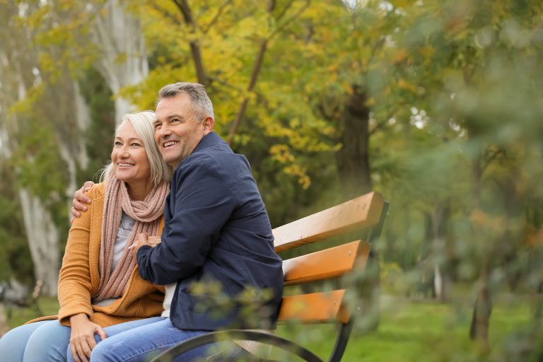 A senior couple embraces and smiles while sitting on a bench in autumn.