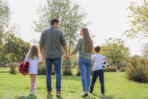 A family of two adults and two children walk together in a park with a soccer ball on a sunny, fall day. Photo by Family Moments.