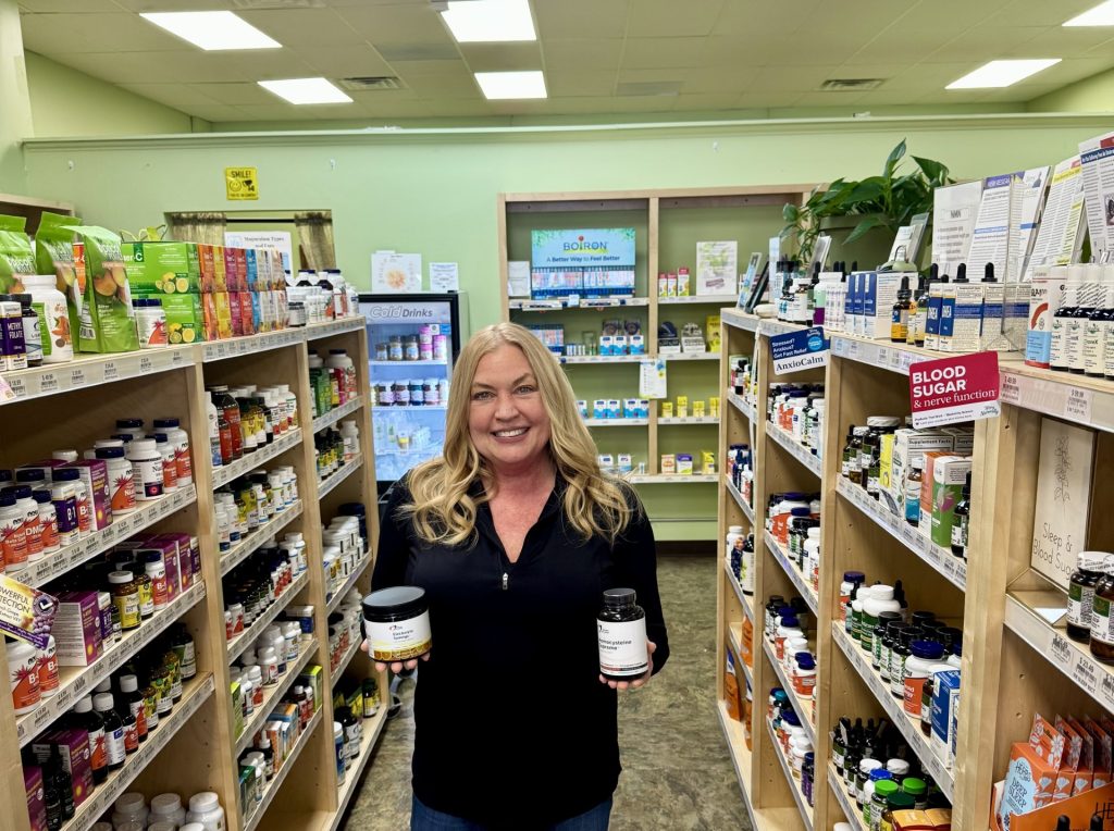 Debbie Pastrano, wellness coach at Rebekah's Grand Blanc, poses in store holding several practitioner-grade supplement bottles.