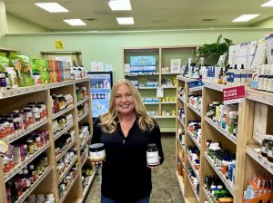 Debbie Pastrano, wellness coach at Rebekah's Grand Blanc, poses in store holding several practitioner-grade supplement bottles.