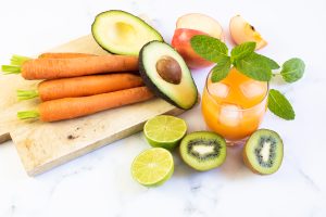Fresh fruits and vegetables scattered on a cutting board and marble countertop, with a glass of fresh orange juice. Photo credit: Healthy Living.