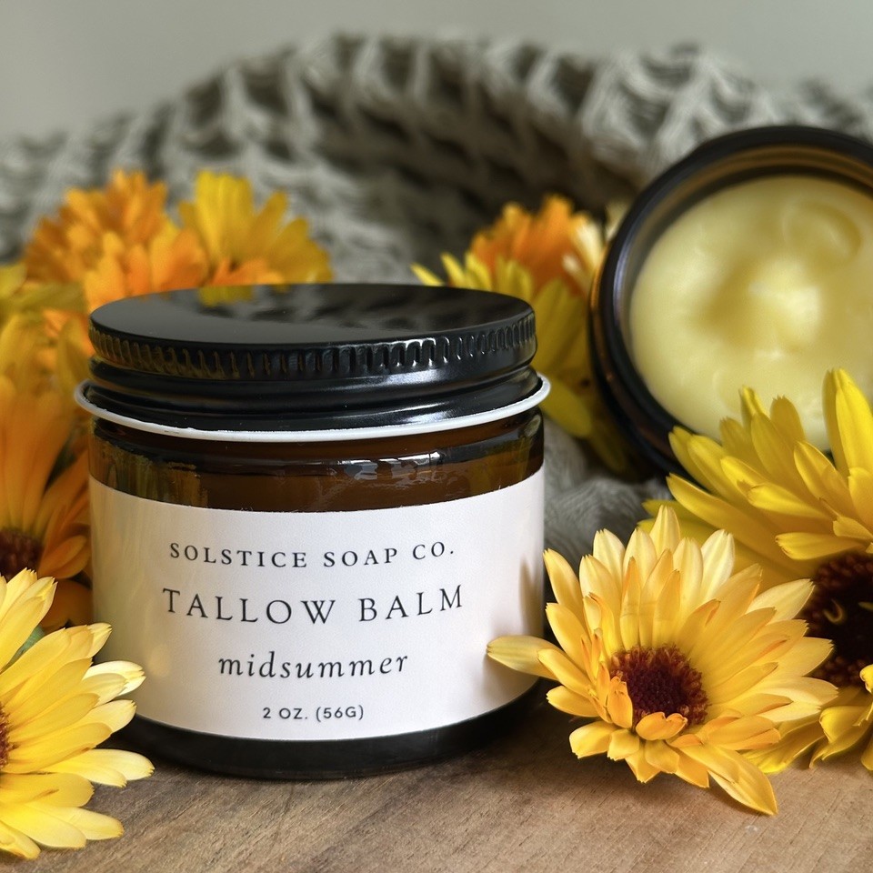 Tallow Balm Midsummer product on display with various summer flowers.